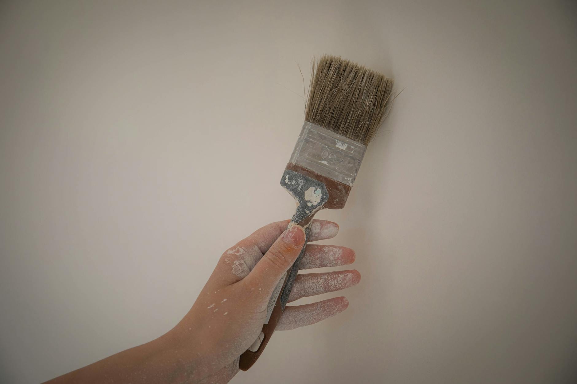 Ręka malująca białą farbą gładką ścianę podczas prac remontowych